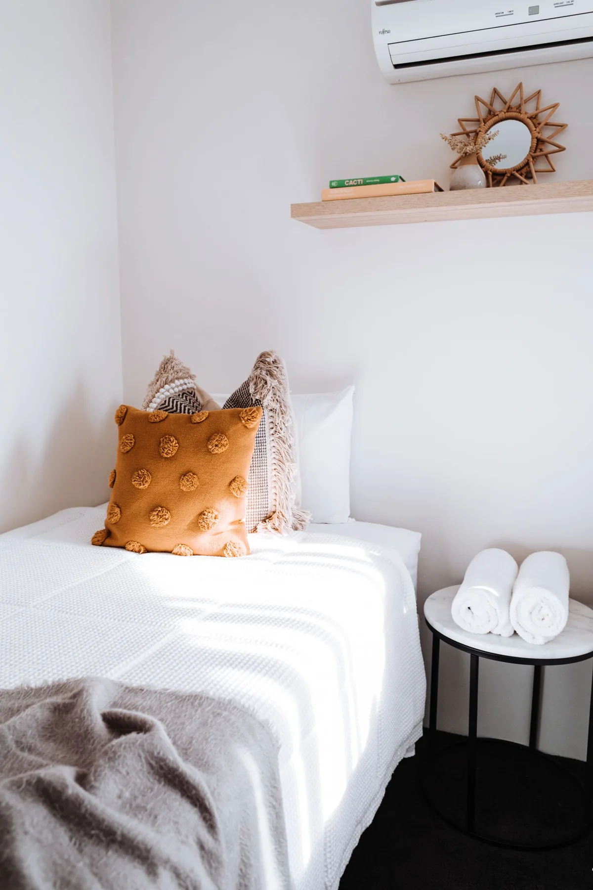 Fresh white bedding and rolled towels in a bright guest bedroom.